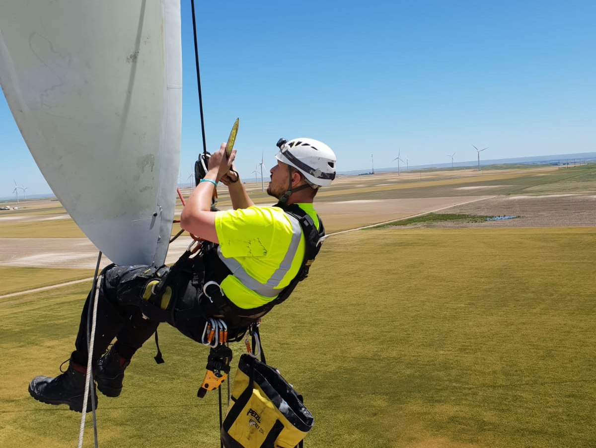 A man is climbing a wind turbine while wearing a helmet.