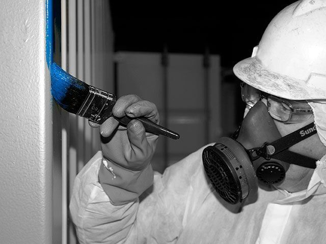 A man wearing a face mask is painting a wall with a brush.