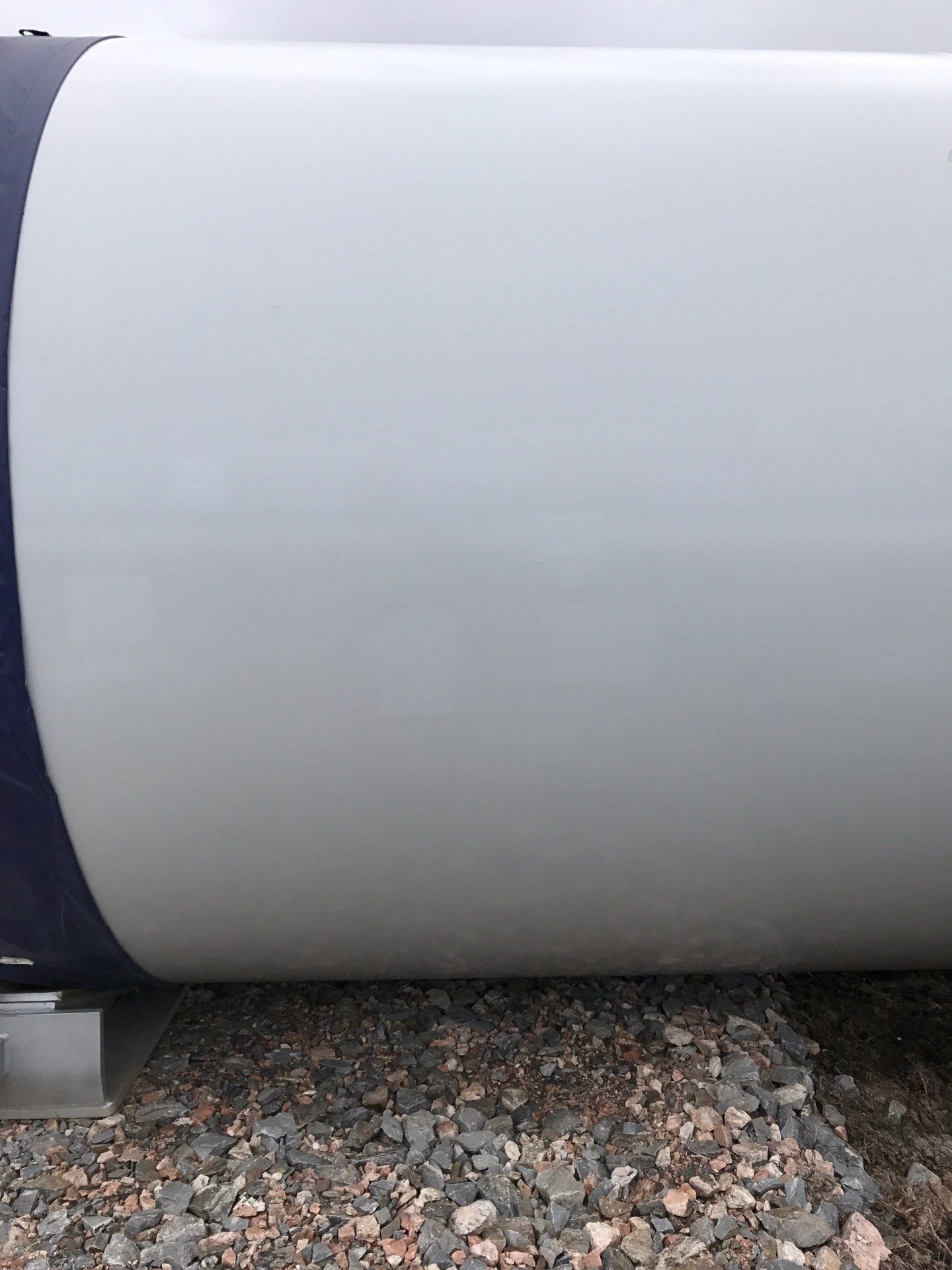A large white wind turbine blade is sitting on top of a pile of gravel.