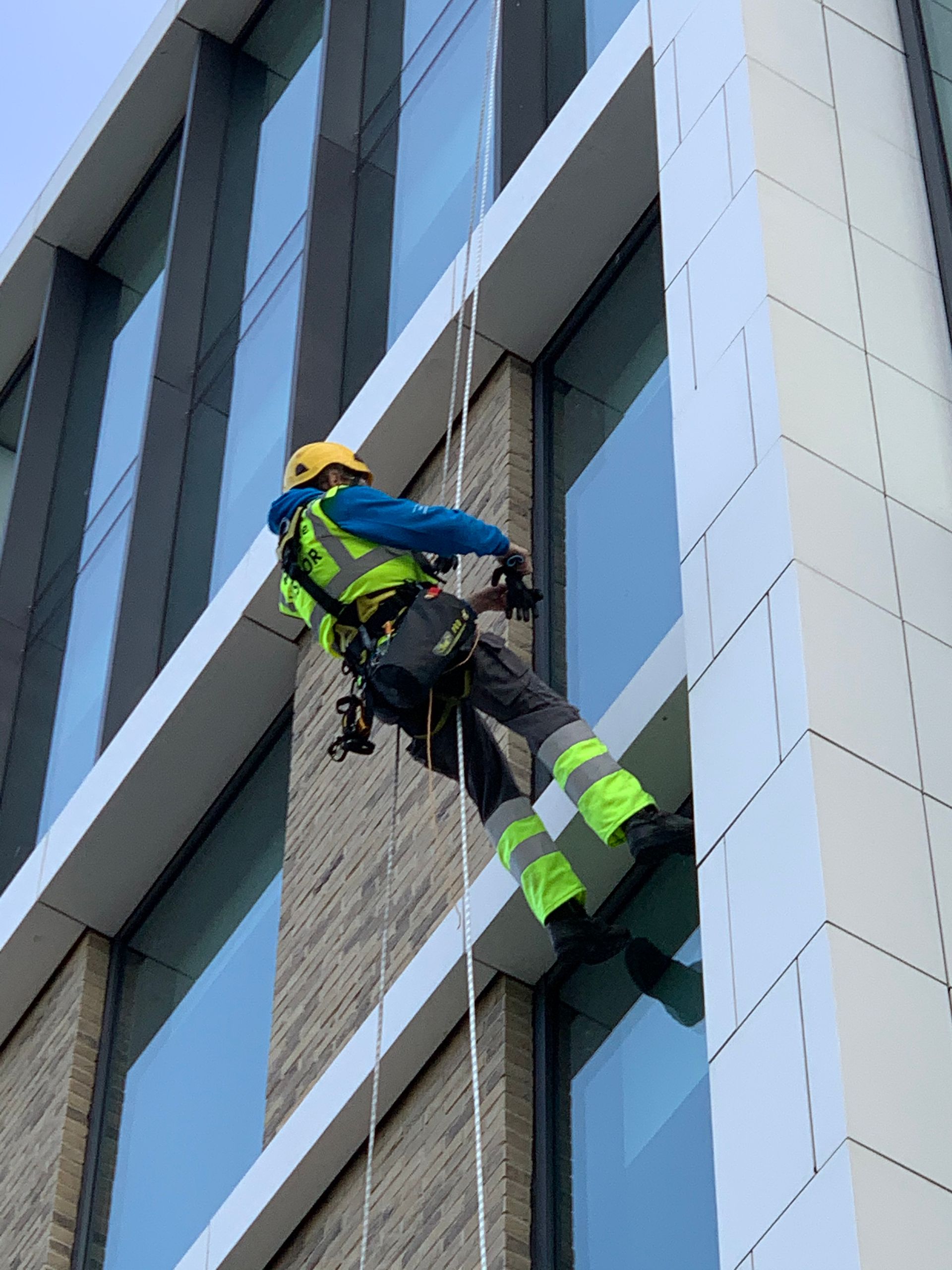 A man is climbing up the side of a building cleaning cladding.