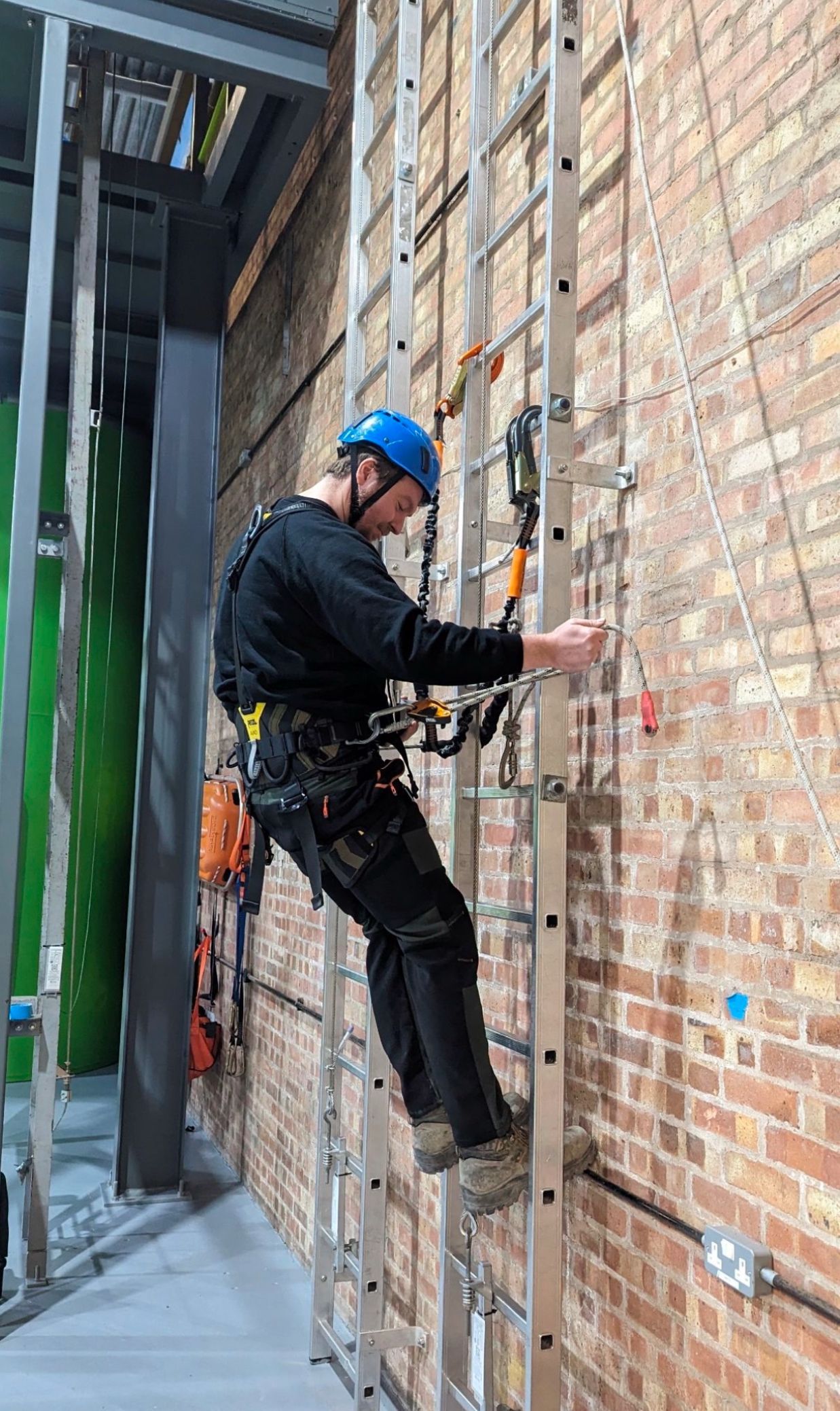 A man is climbing a ladder up a brick wall.