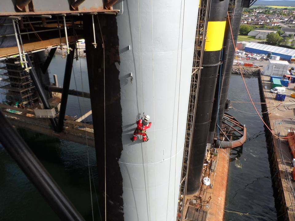 A man is climbing up a very tall leg of a oil rig structure