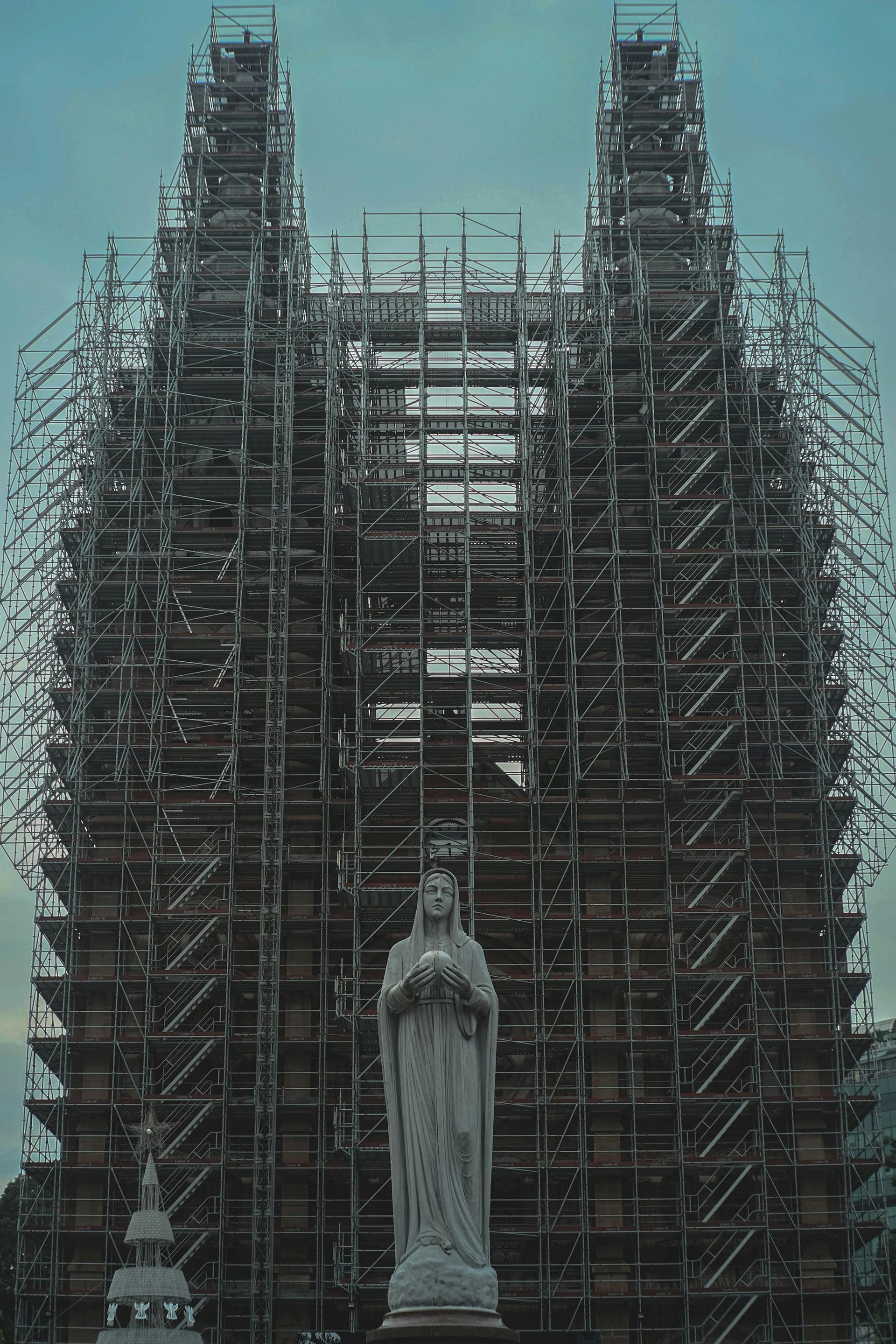 A statue of a woman is standing in front of a building covered in scaffolding.