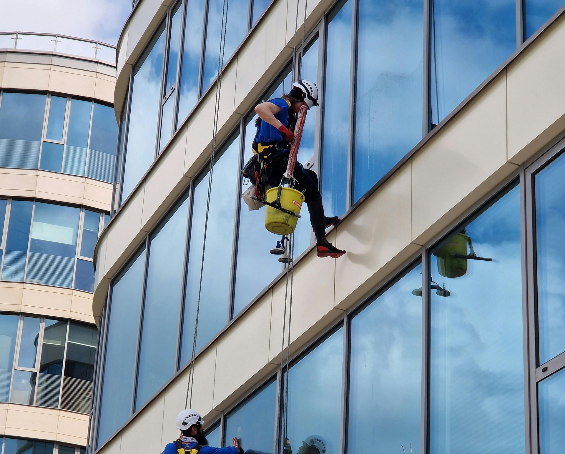 Two men are maintenance cleaning the exterior windows of a tall building using ropes.