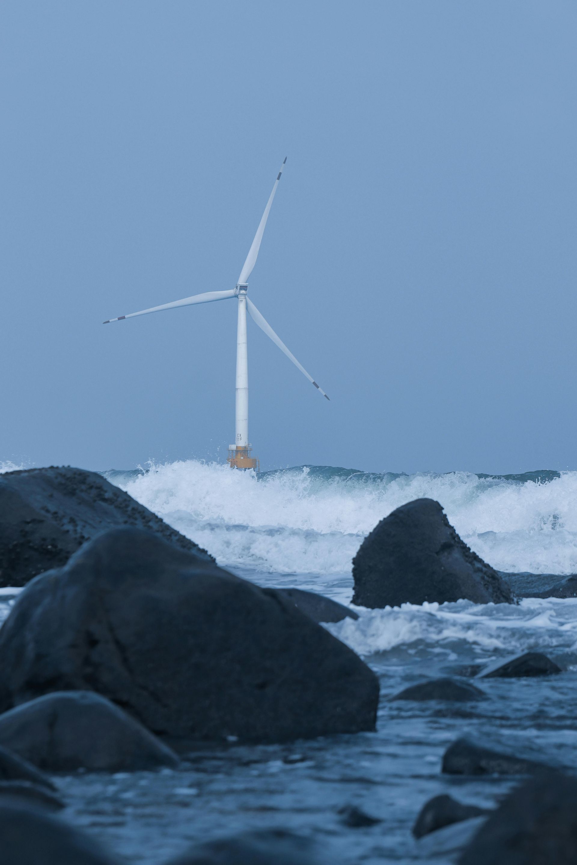 A wind turbine is sitting on top of a rocky beach next to the ocean.