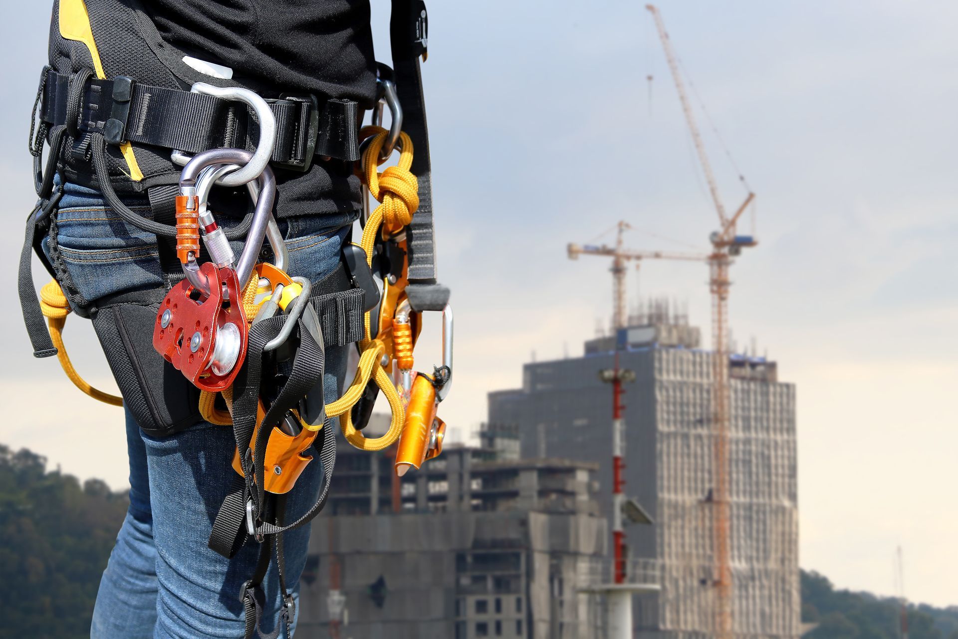 A person wearing a safety harness is standing in front of a building under construction