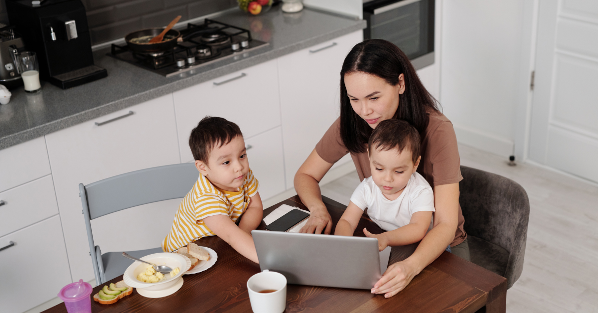 A woman is sitting at a table with two children and using a laptop computer.