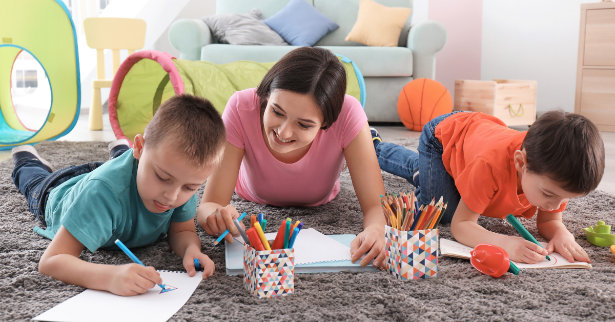 A woman and two children are laying on the floor drawing with pencils.
