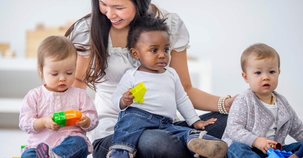 A woman is sitting on the floor with three babies playing with toys.
