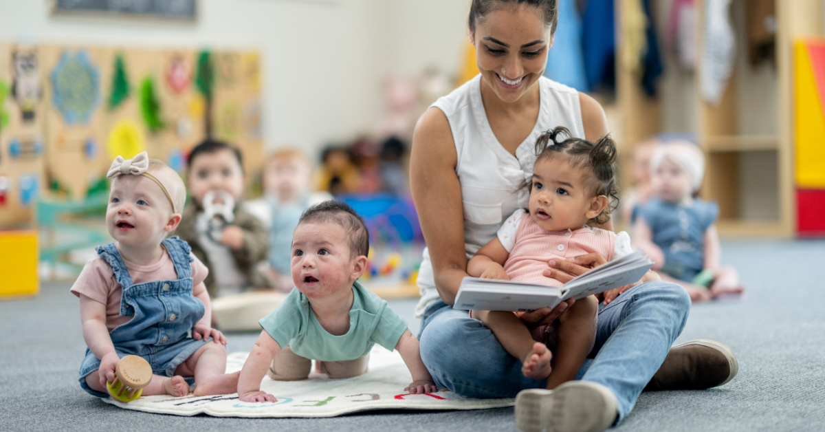 A woman is sitting on the floor reading a book to a group of babies.