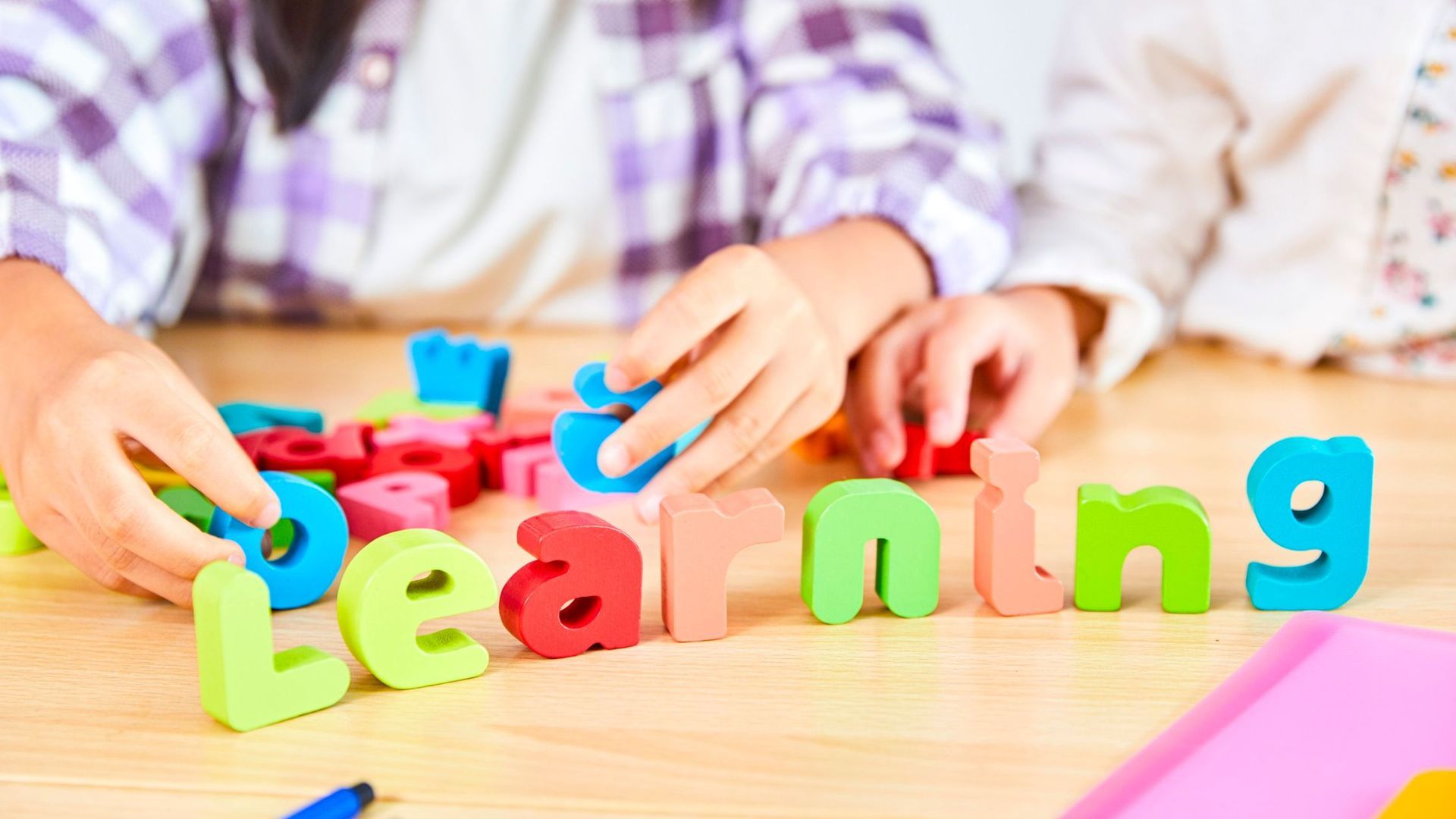 Hands arranging colorful wooden letters spelling 