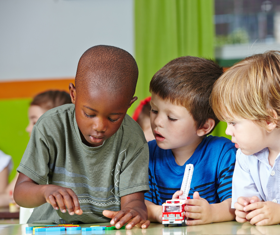 Three young boys are playing with a toy fire truck on a table.