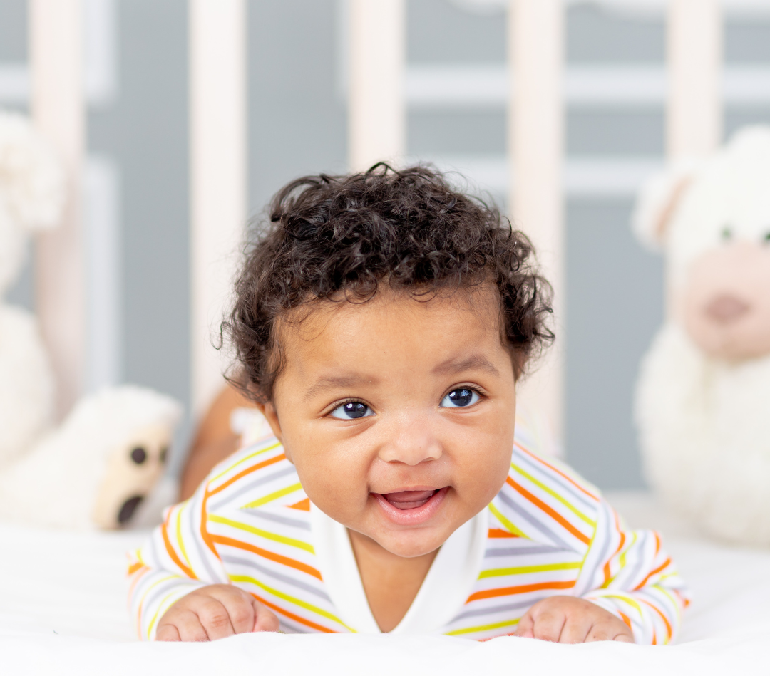 A baby is laying on his stomach in a crib and smiling.