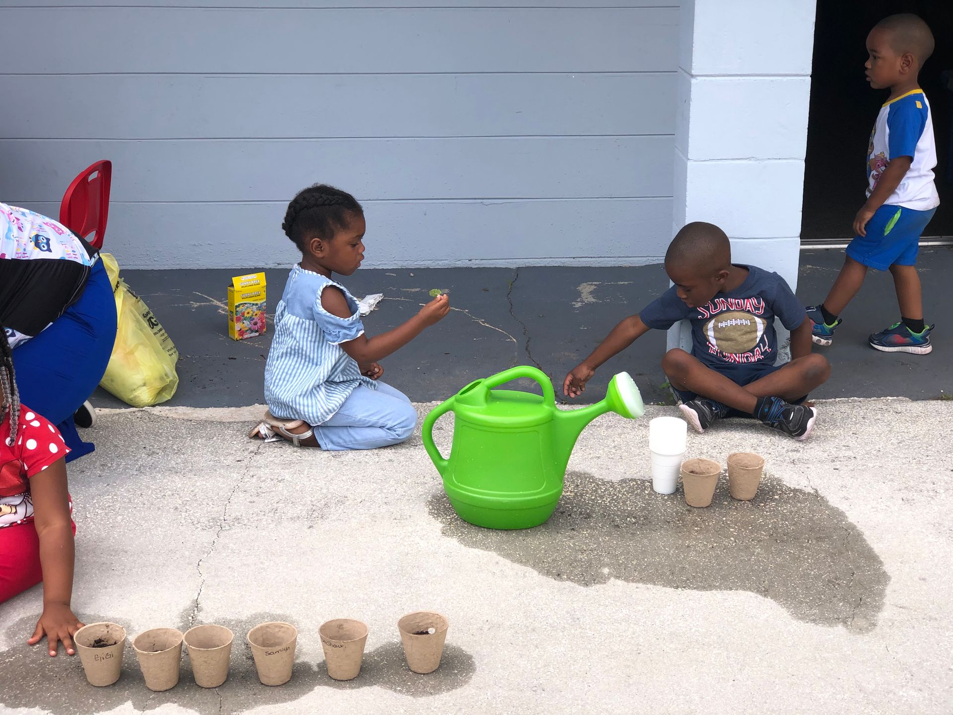 A group of children are playing with a watering can and pots.