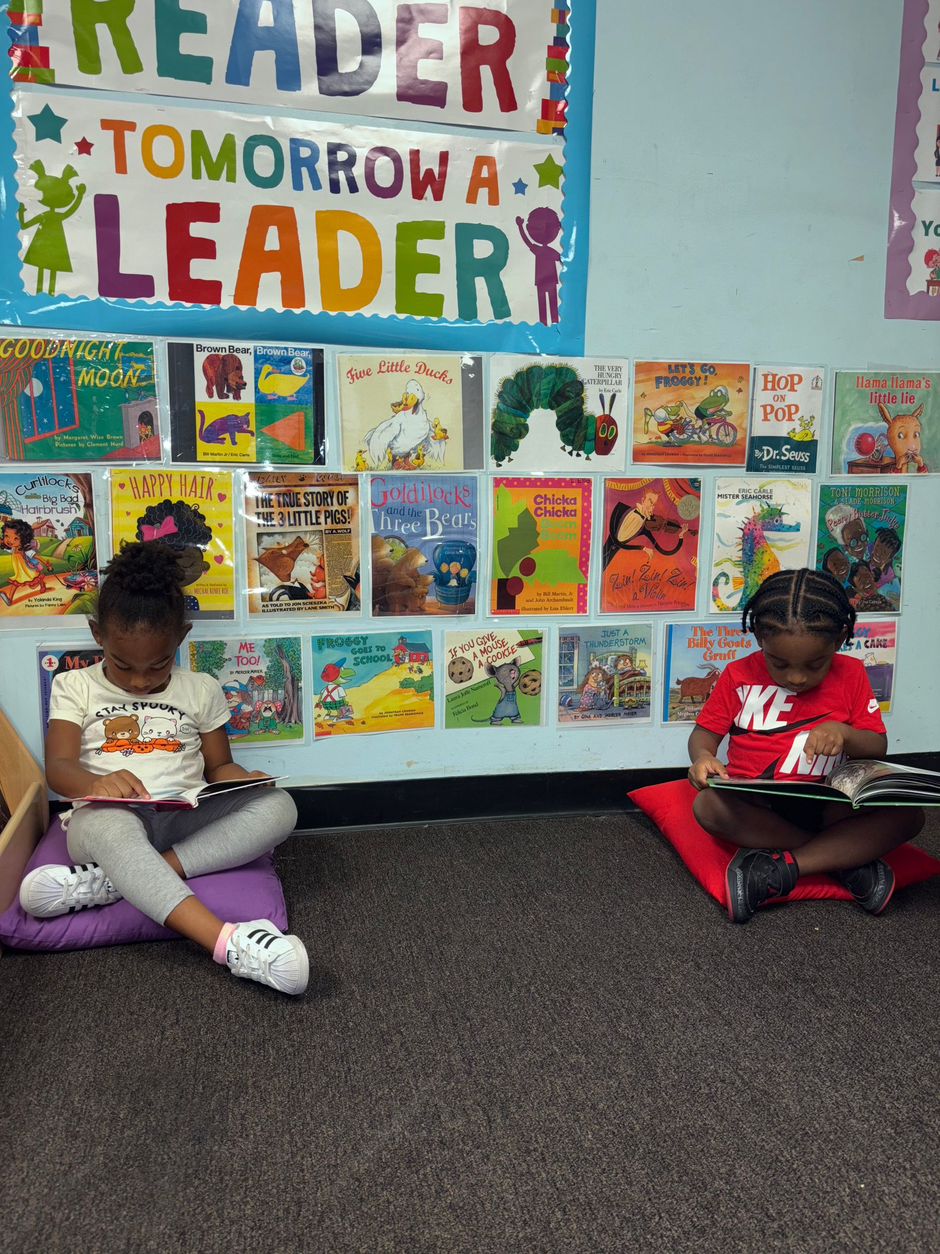 Two young girls are sitting on pillows reading books in a library.