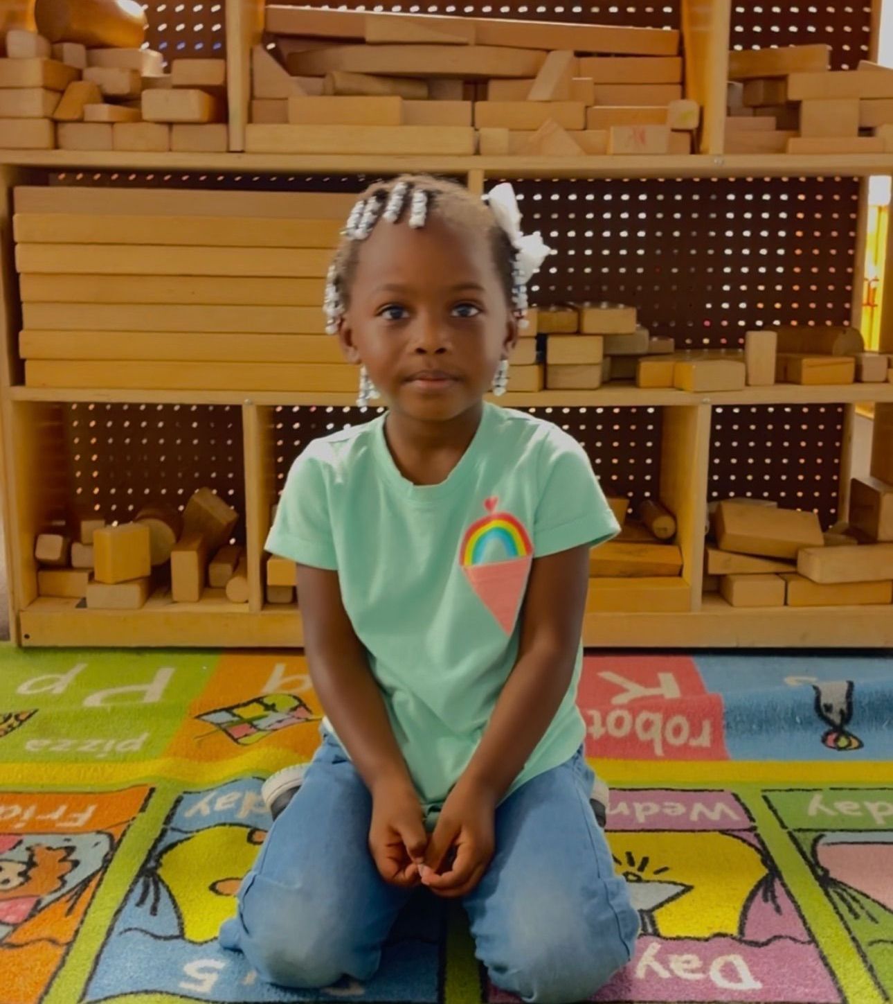 A little girl is kneeling down in front of a shelf full of wooden blocks