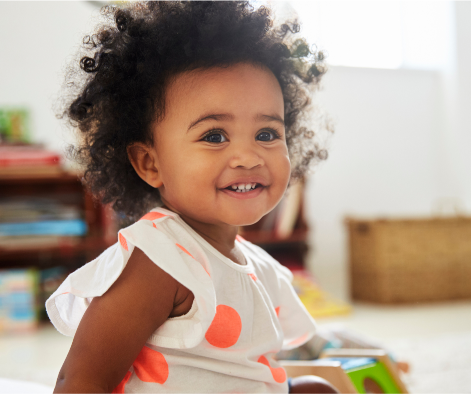 Smiling child with curly hair in a polka dot shirt, indoors.