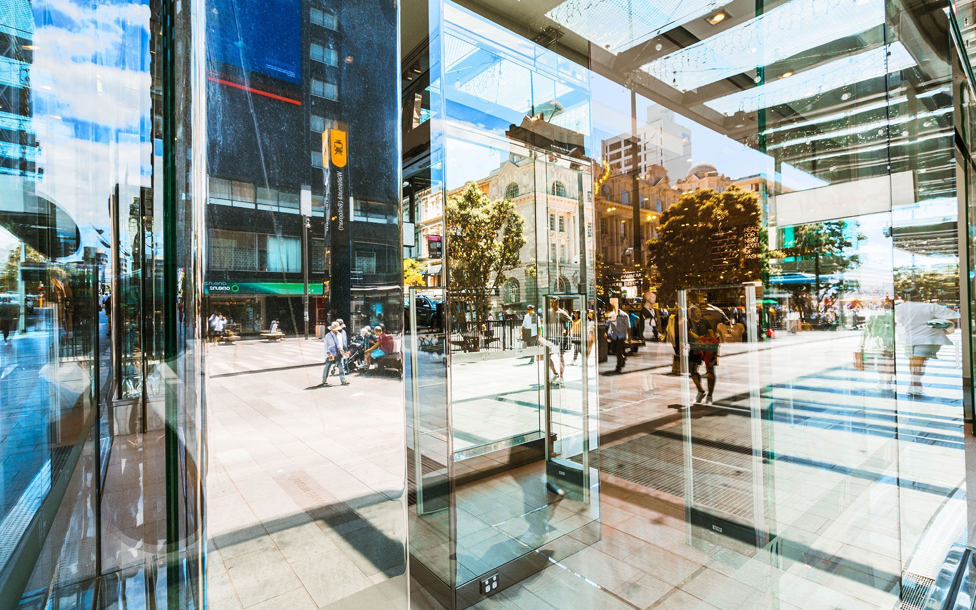 Glass storefront reflecting city street scene with pedestrians and buildings.