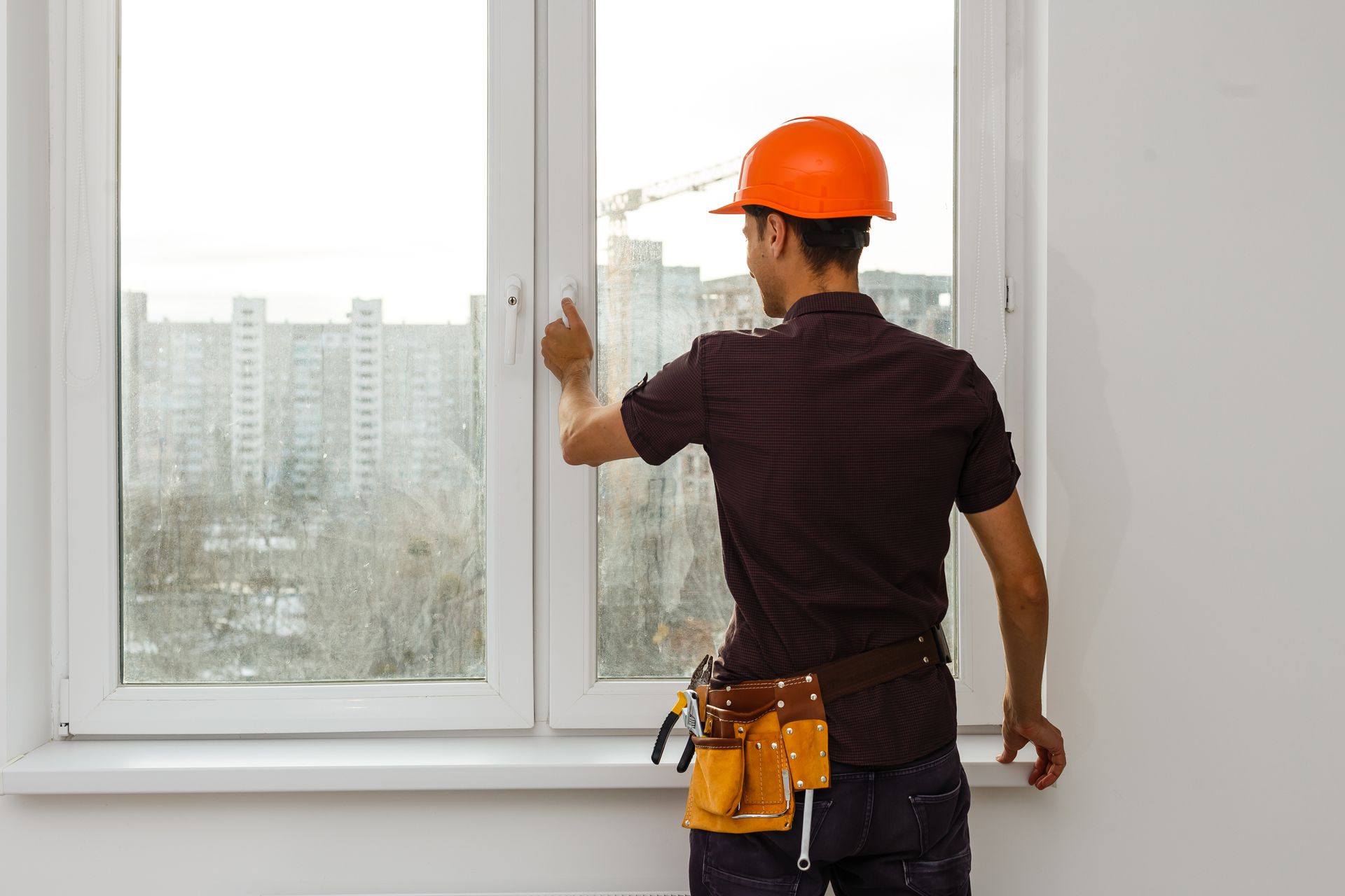 Man in hard hat and vest inspecting a window for a professional window glass repair assessment.