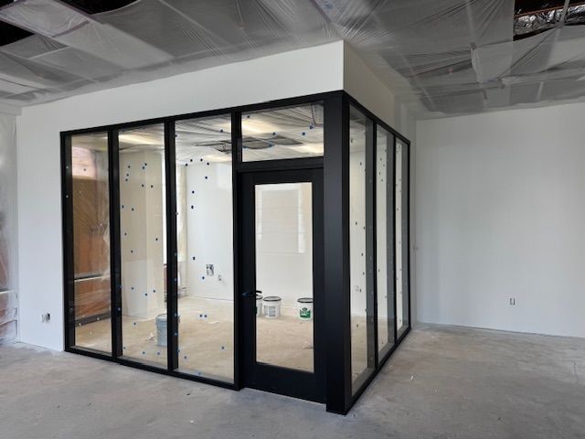 A glass-walled office under construction, featuring black frames, a door, and a white ceiling.