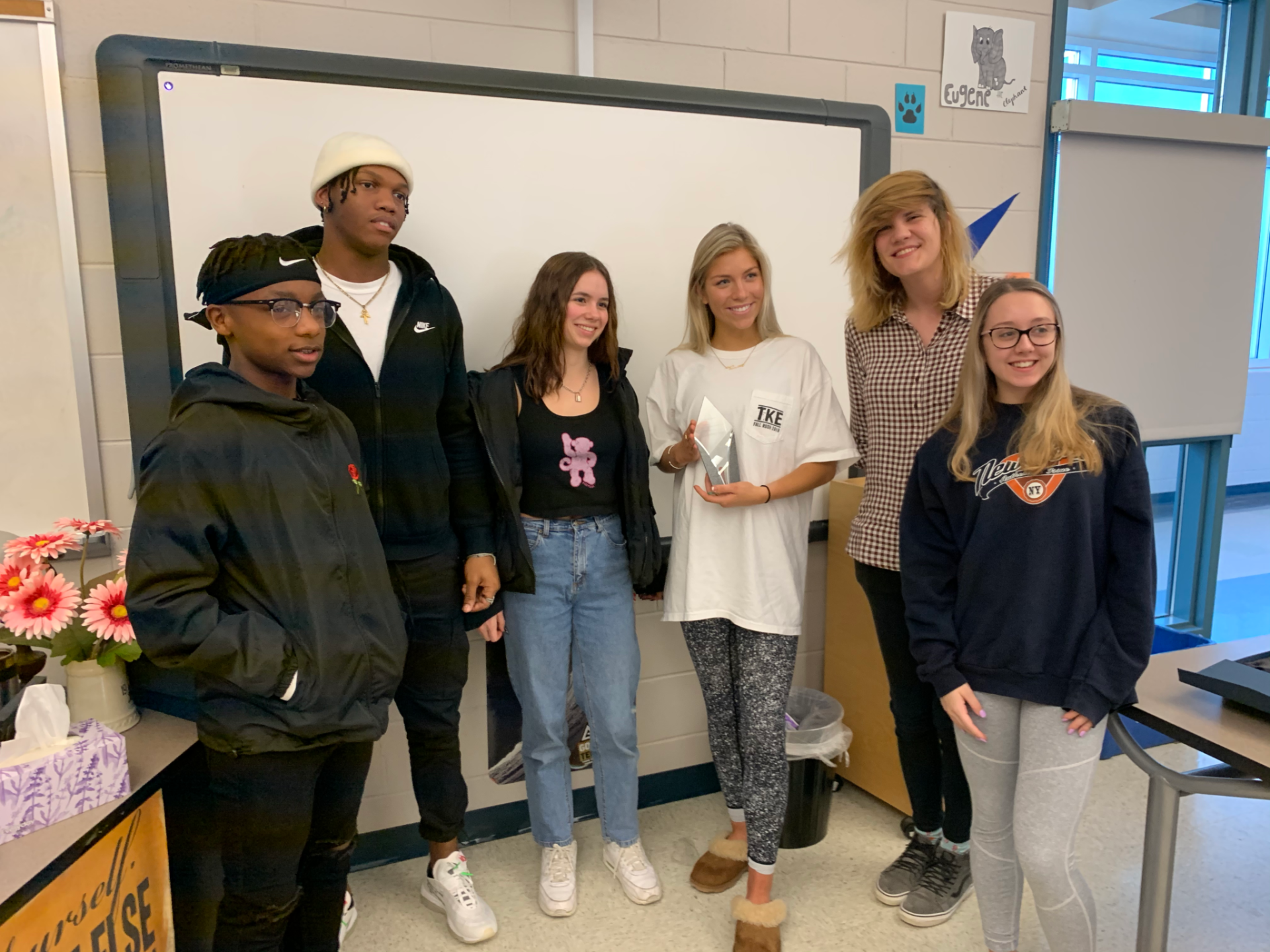 A group of people are standing in front of a whiteboard in a classroom.