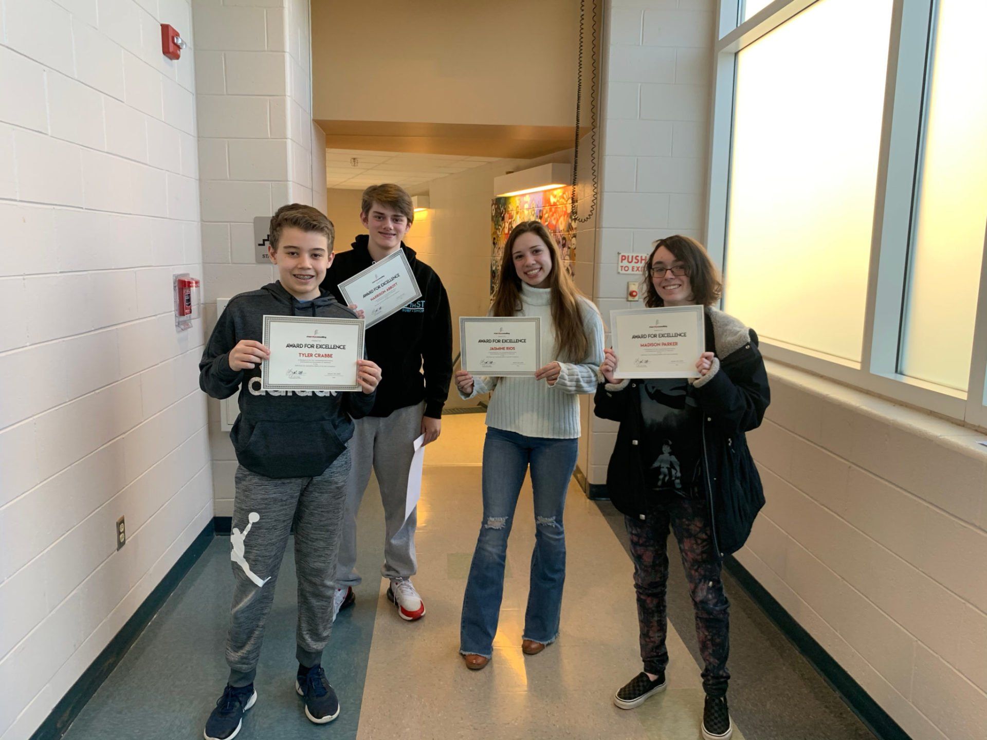 A group of young people are standing in a hallway holding certificates.