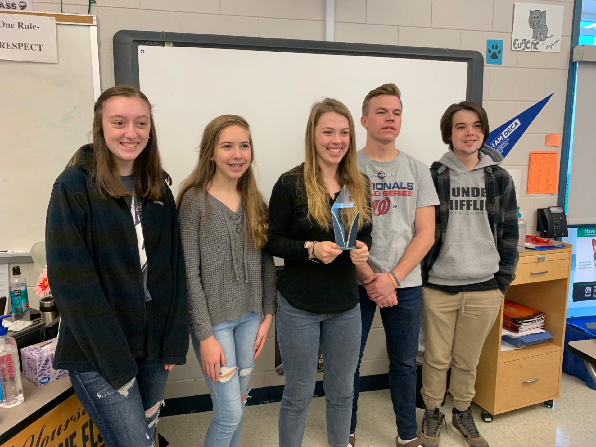 A group of young people are standing in front of a whiteboard in a classroom.