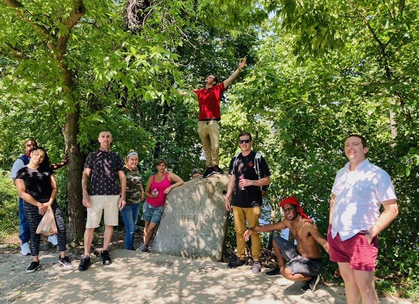 A group of people are standing around a large rock in the woods.