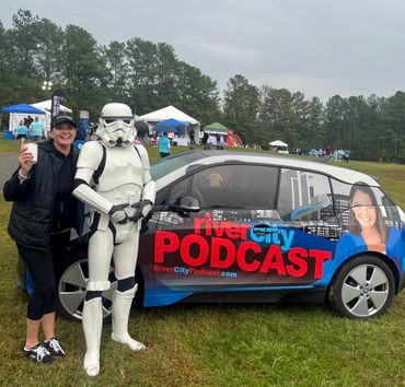 Woman and Stormtrooper pose with a River City Podcast car at an outdoor event.