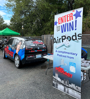 Car and sign promoting a podcast giveaway for AirPods. Outdoor setting.