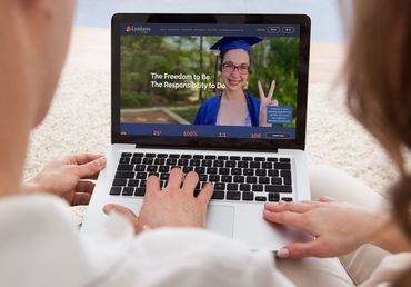 Couple using a laptop, viewing a website with a woman in a graduation cap, outside.