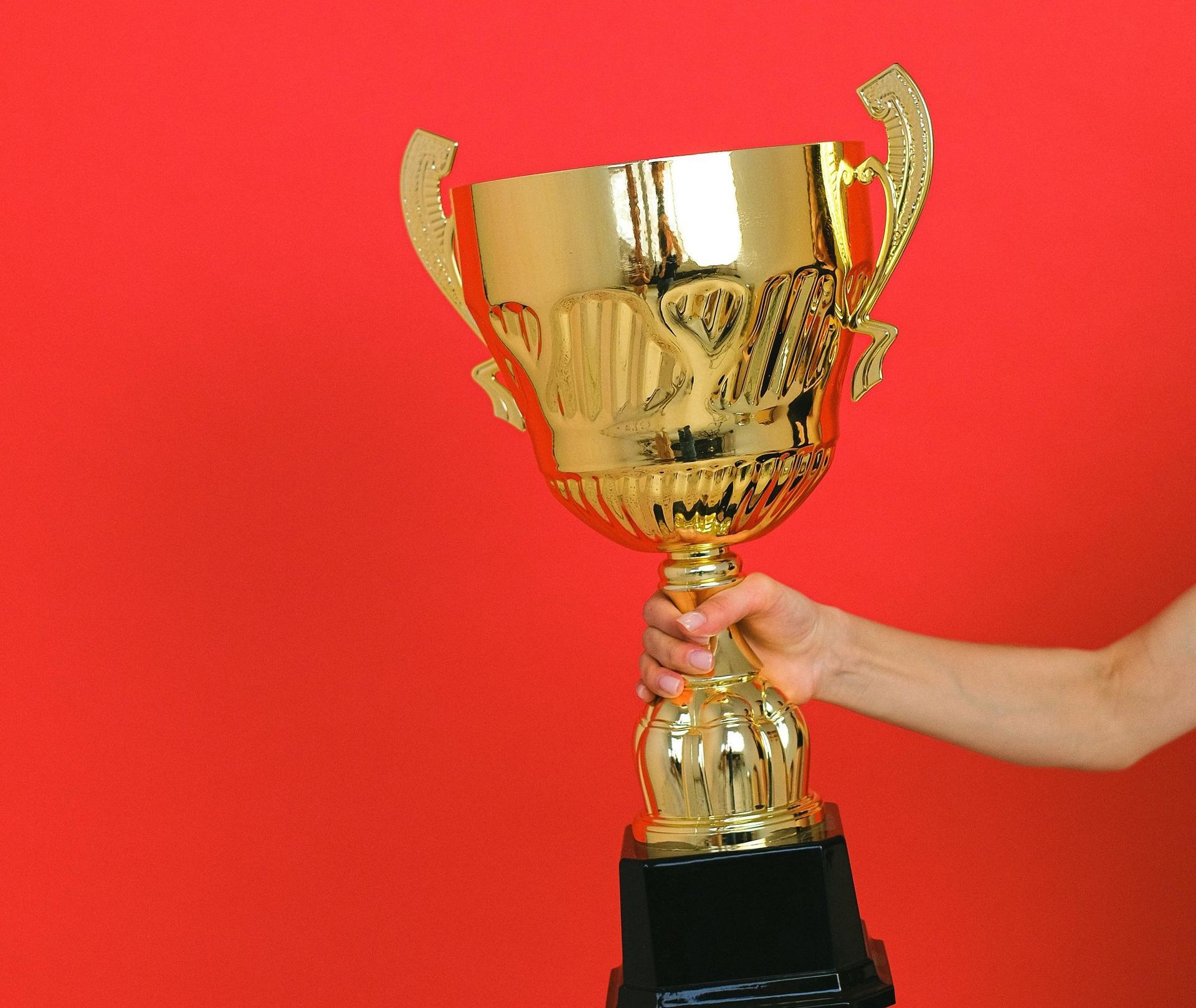 A person is holding a gold trophy on a red background.