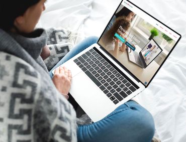 Woman using laptop in bed, website on screen.