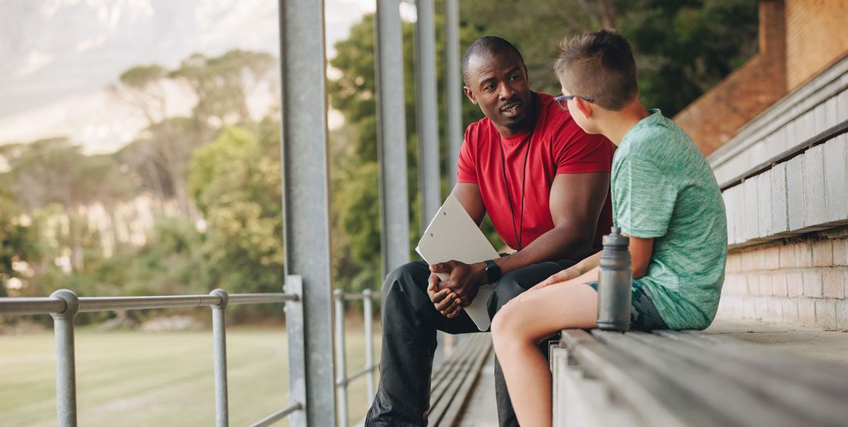 A man and a boy are sitting on the bleachers talking to each other.