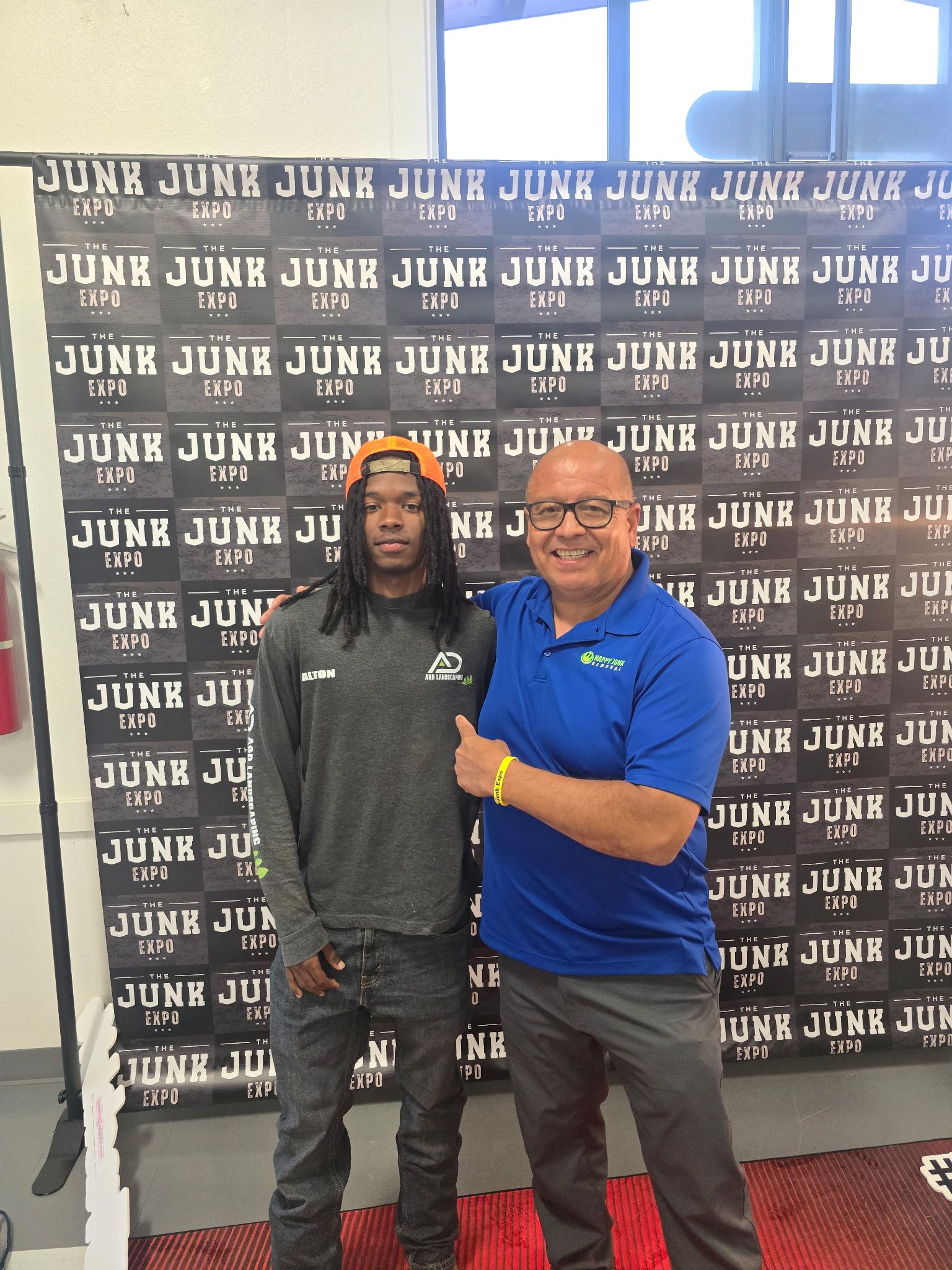 Two junk removal owners posing in front of a banner with 