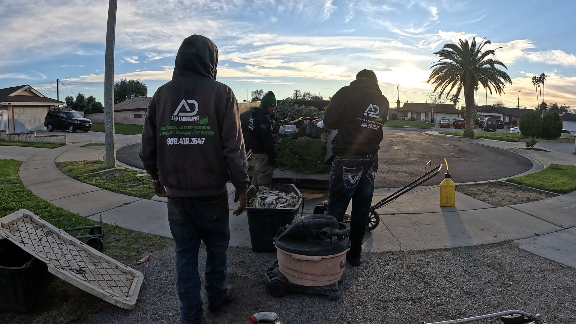 A&D Crew in our hoodies move materials on a residential street with a circular driveway; cloudy sky.