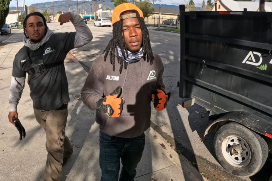 A&D Crew next to our trailer. One flexes arm; the other gestures with thumbs up. Both wear work clothes.