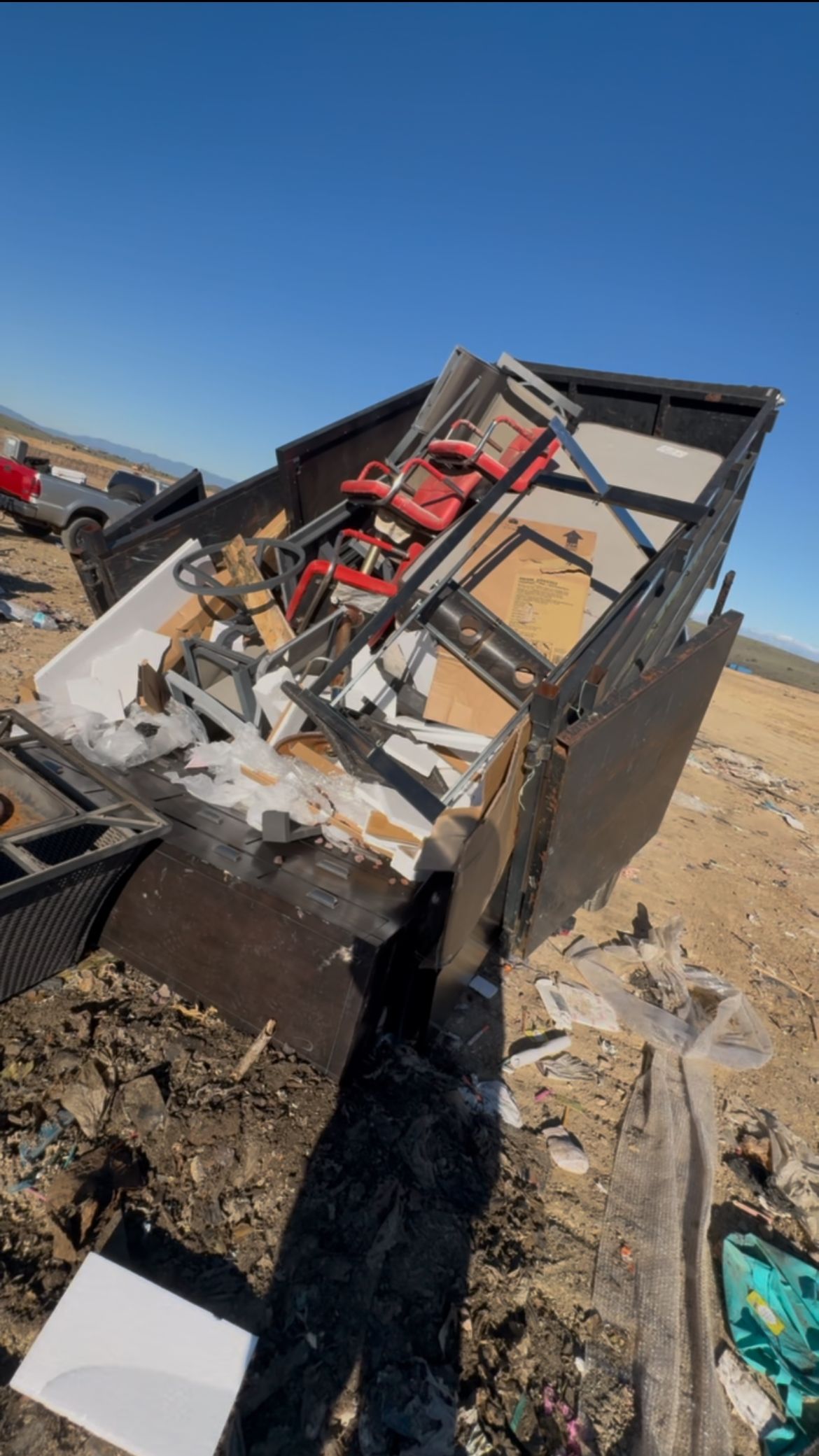 Dumpster filled with debris, including a red saw and broken construction materials, outdoors on a sunny day.