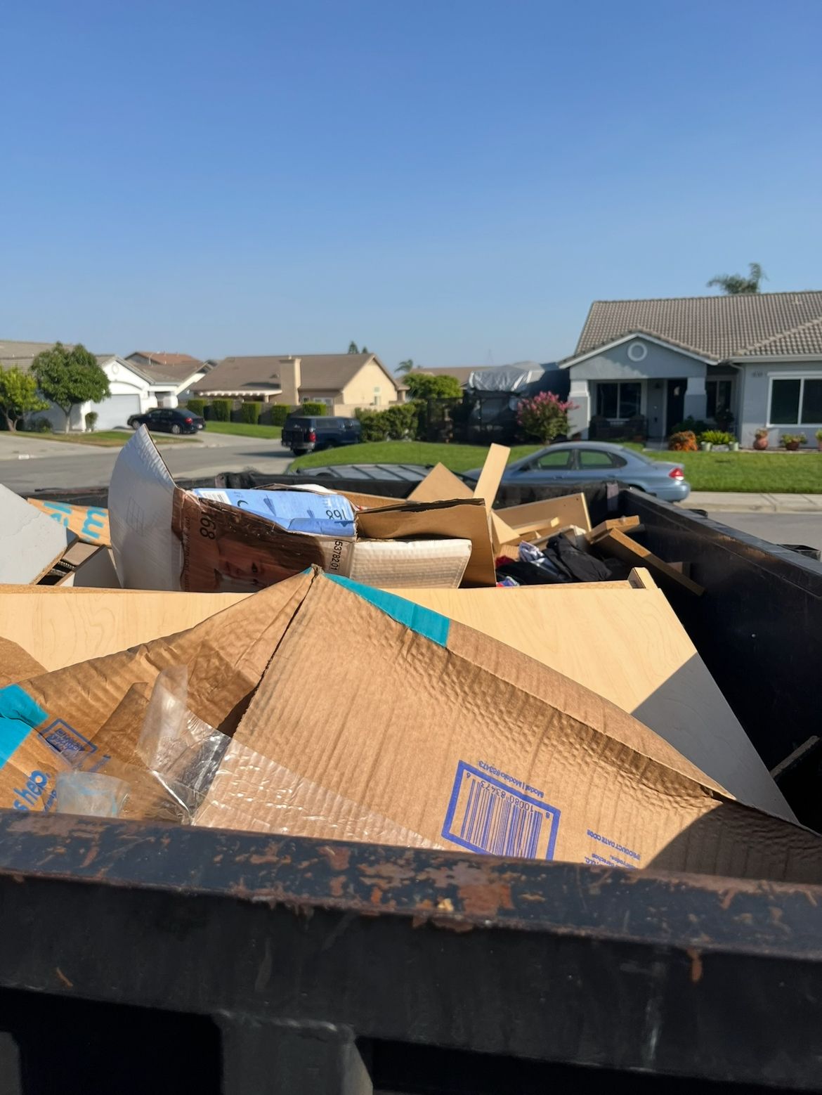 Dumpster filled with cardboard boxes, in a residential neighborhood on a sunny day.