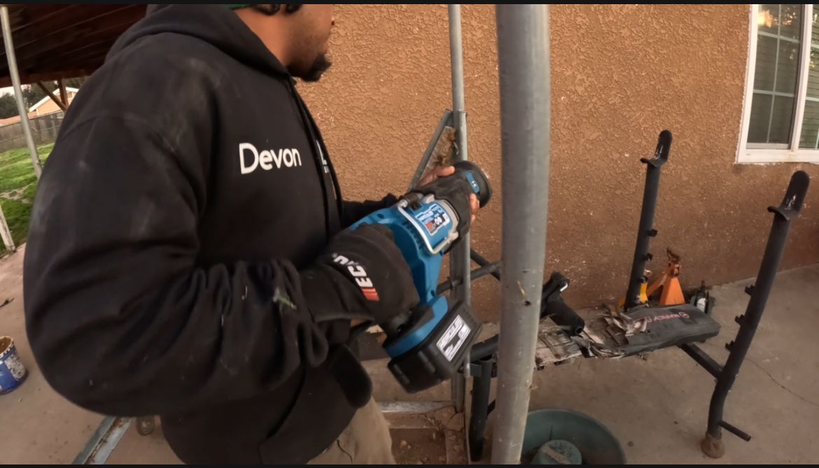 A&D Demo in ourhoodie using a reciprocating saw on a metal pole outdoors.