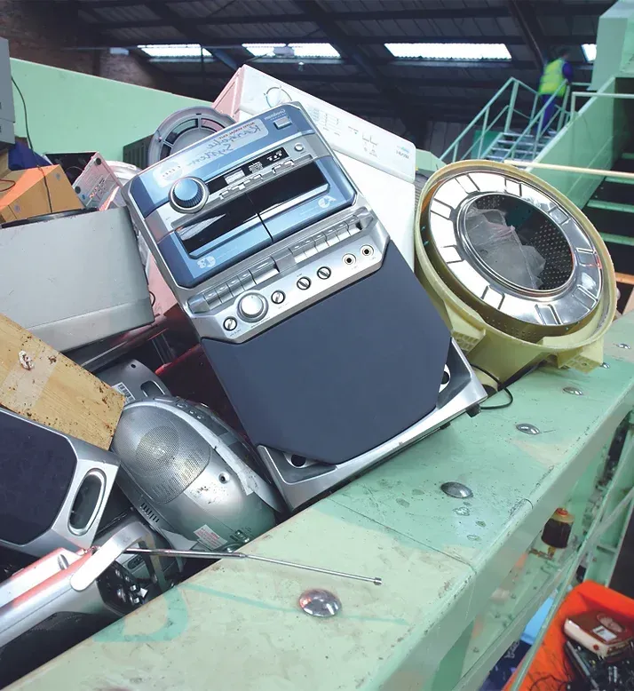 A pile of discarded electronics at a recycling facility, including a stereo system and a clock.
