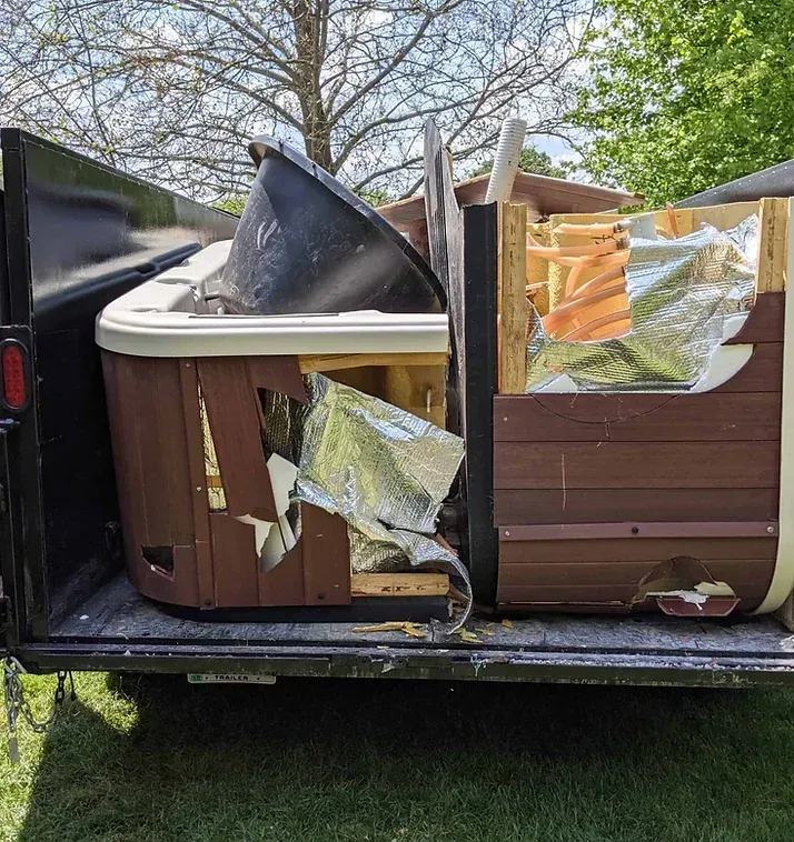 Deconstructed hot tub loaded in a black trailer, revealing wood, insulation, and the tub shell.