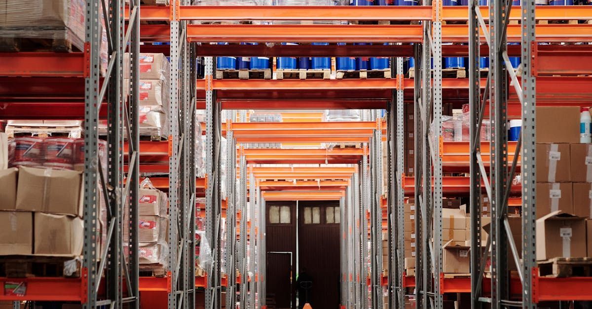 Warehouse interior with rows of orange shelving, stacked boxes and pallets, leading to a closed door.