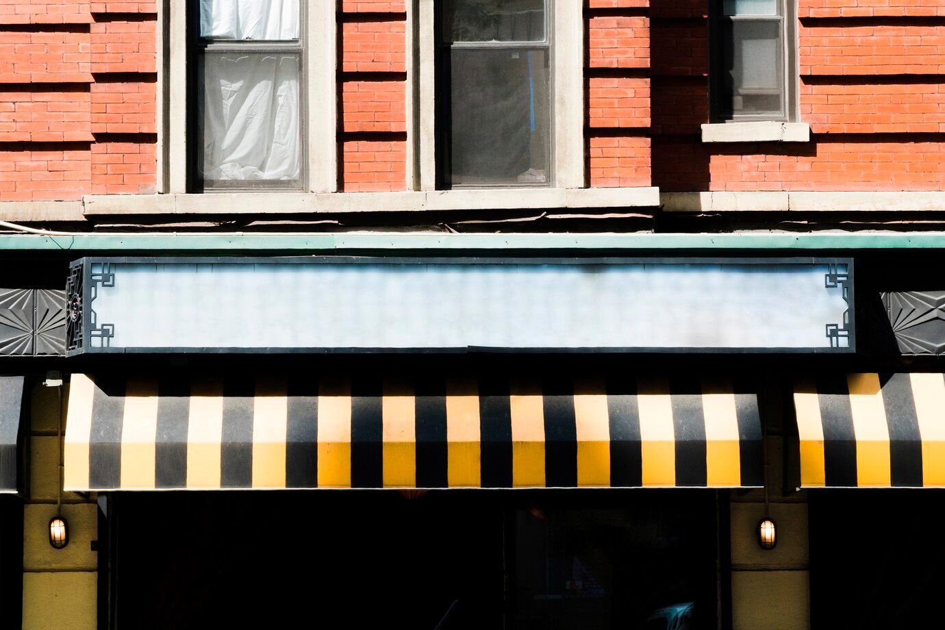 Storefront with blank sign, brick building, striped awning, and two windows.