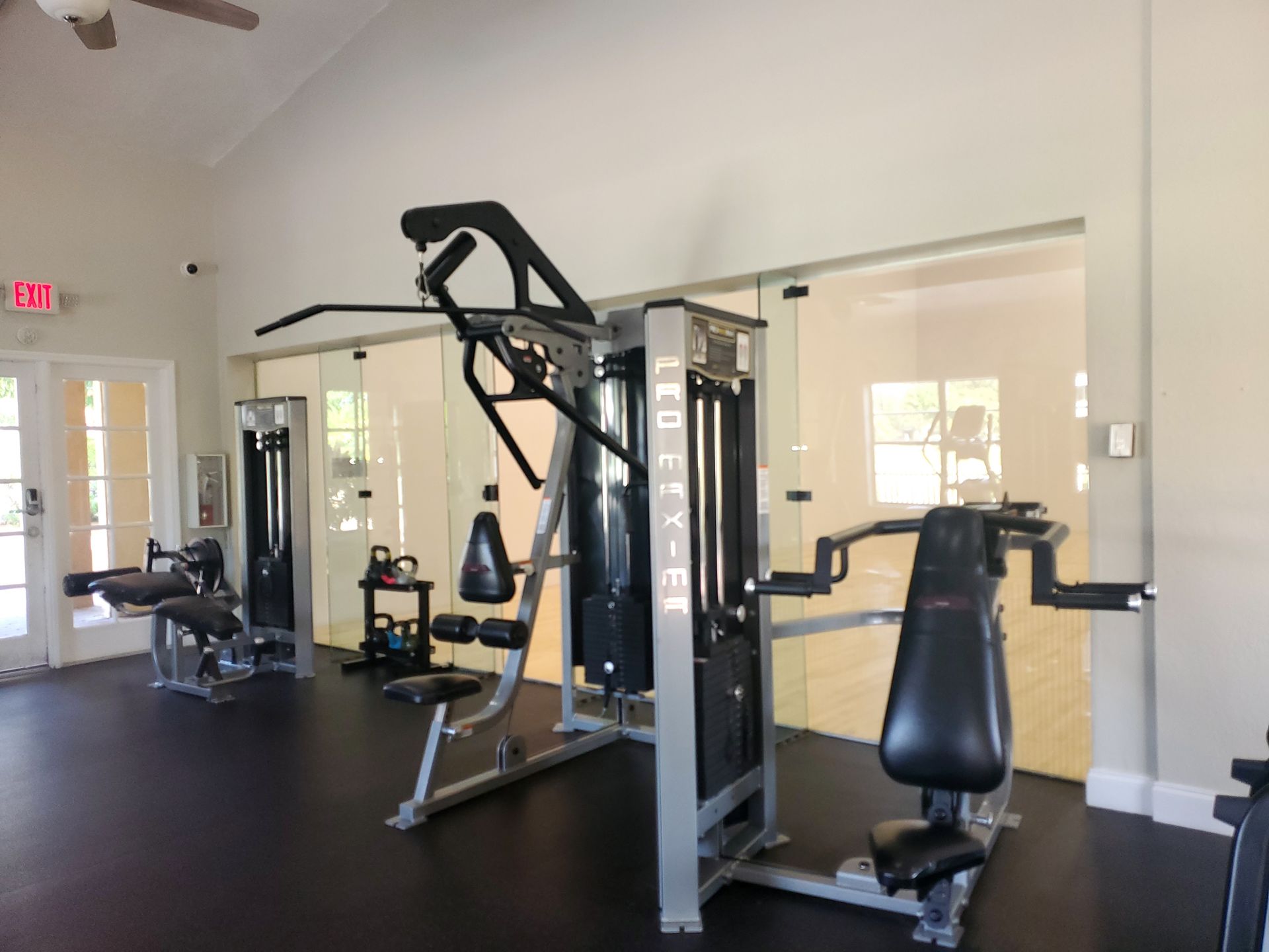Gym equipment in a fitness room with black floor, glass walls, and an exit door.