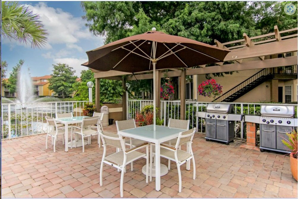 Patio with tables, chairs, grills, and umbrella by a pond with a fountain.
