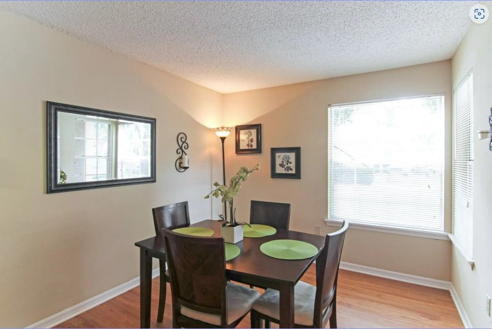 Dining area with dark wood table and chairs, wall mirror, window, and decorative art.
