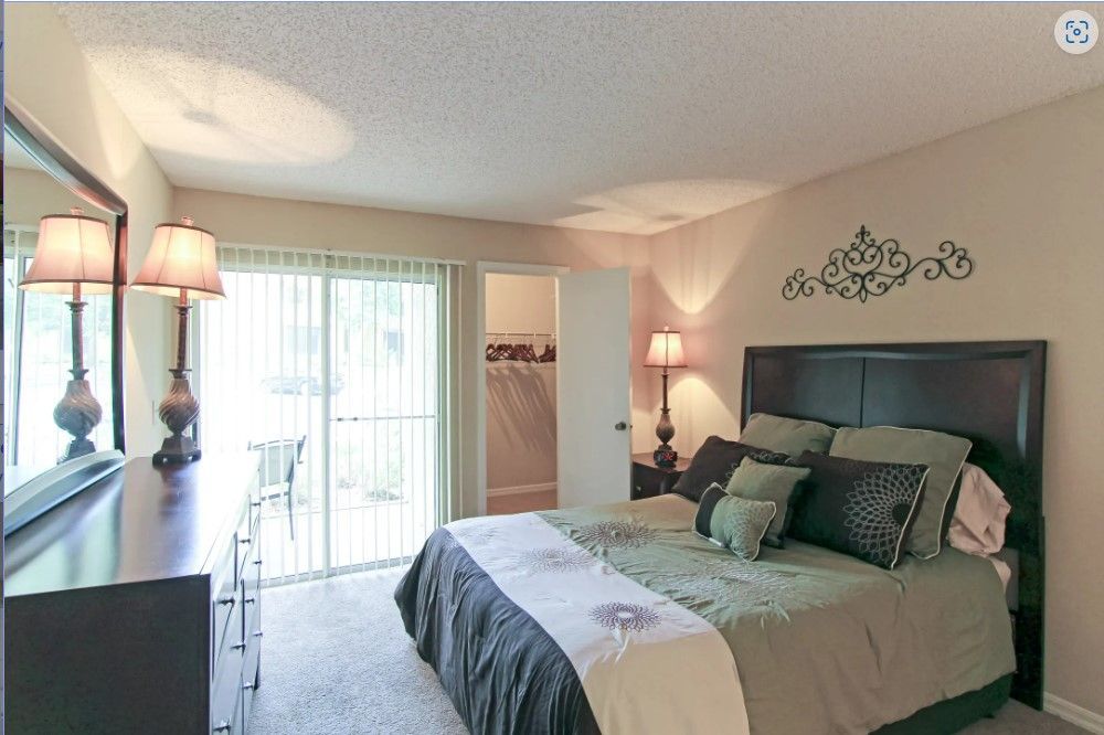Bedroom with dark furniture, bed with green bedding, and a sliding glass door.