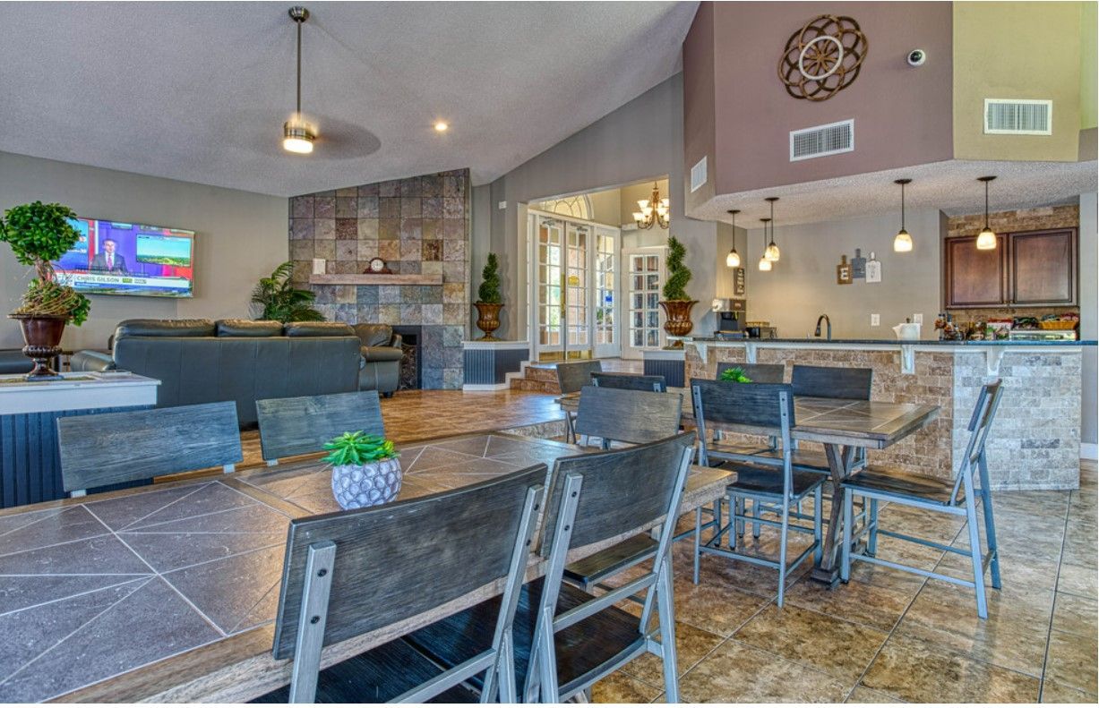 Spacious, modern lounge with long dining table, seating, and bar area. Grey, stone accents and decorative pieces.