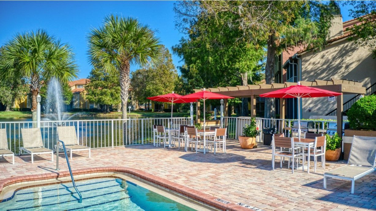 Poolside patio with tables, red umbrellas, lounge chairs, and a fountain.